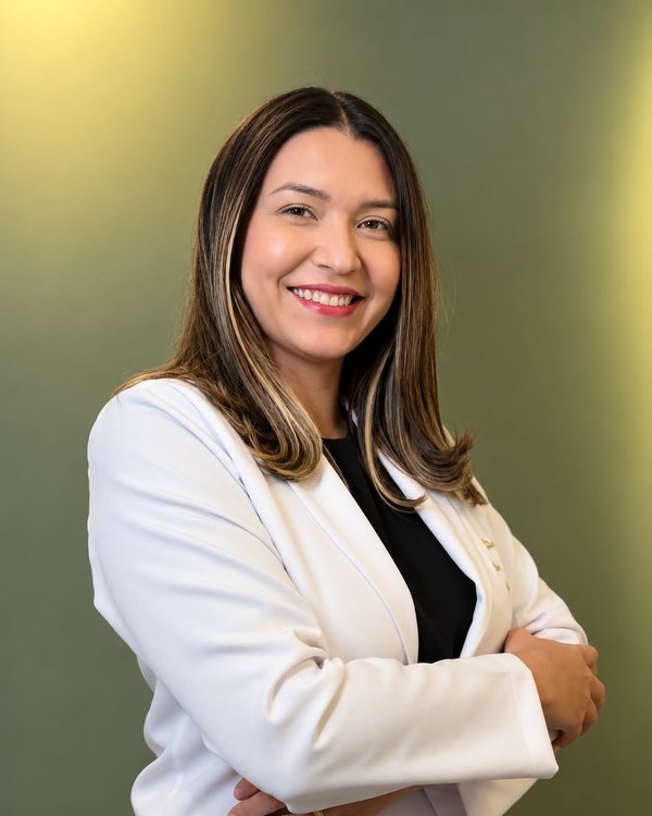 Dra. Anne Julie, oftalmologista, de jaleco branco, sorrindo, de braços cruzados